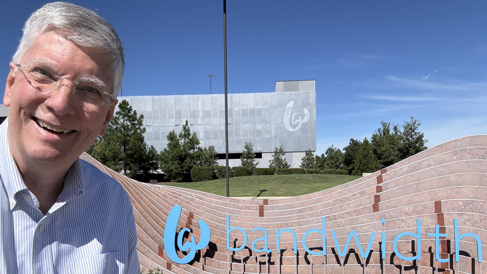 Nicky Smith, founder of Carolina Digital Phone, smiling beside the Bandwidth headquarters sign in Raleigh, North Carolina