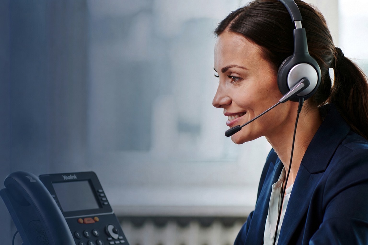 Customer service representative wearing a headset and smiling, with a Yealink desk phone in the foreground