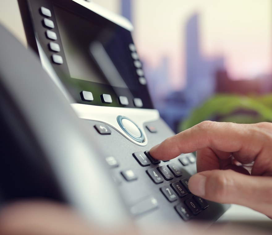 A person dialing a modern VoIP desk phone in an office