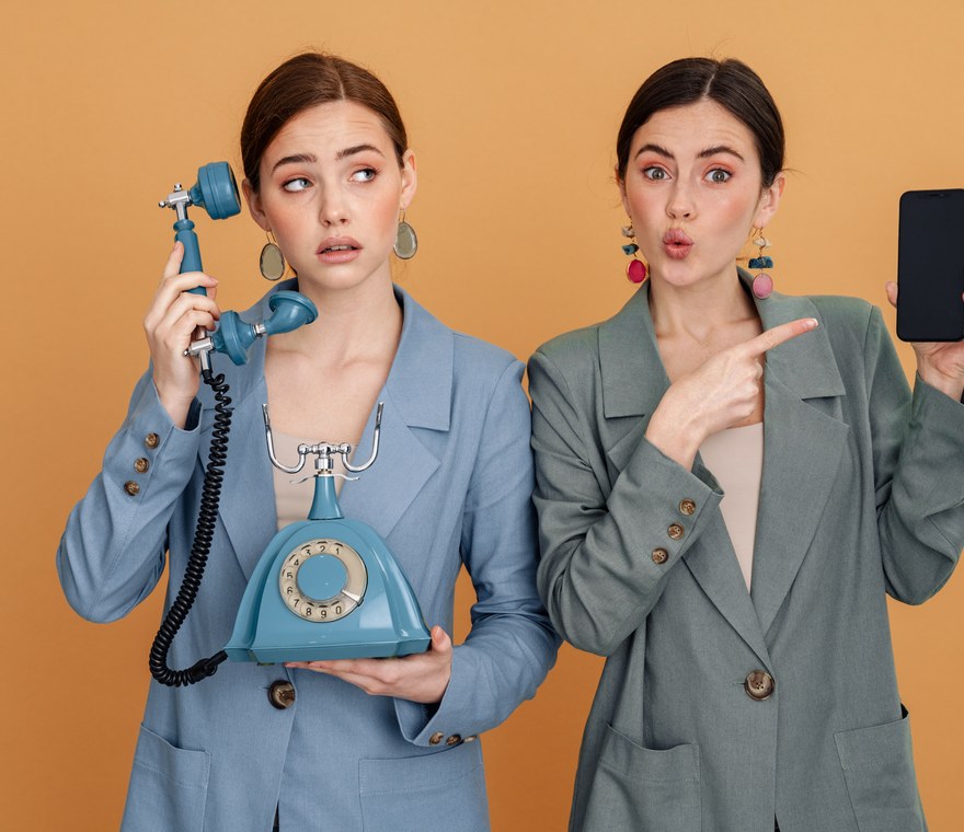 Two professionals comparing an old rotary phone with a modern smartphone