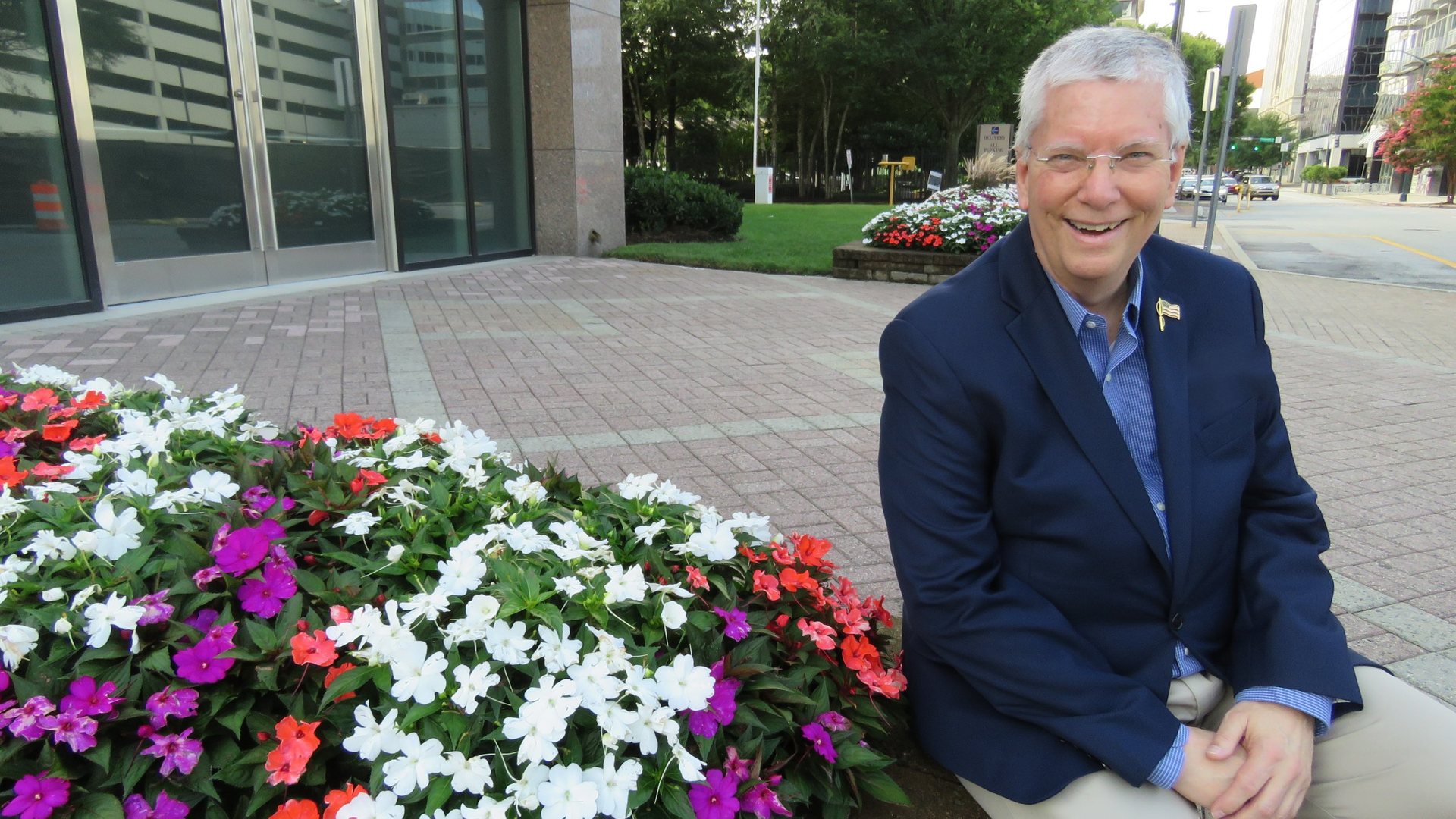Nicky Smith, founder of Carolina Digital Phone, smiling beside a flower bed on a downtown sidewalk