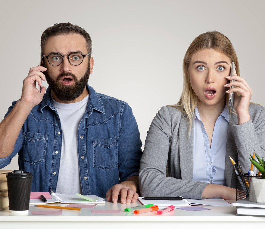 Two business coworkers looking alarmed while on their phones during an office outage