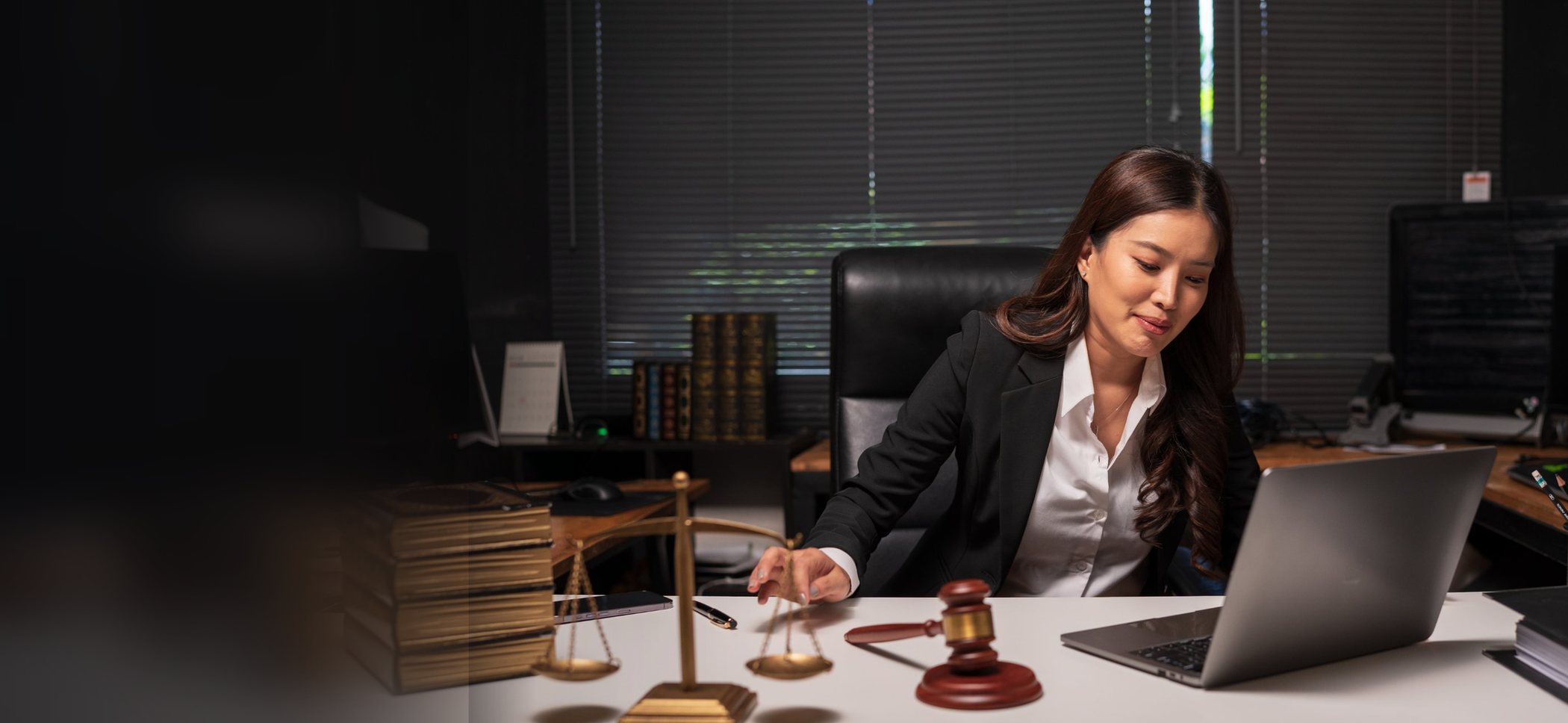 An attorney working at her desk beside law books, the scales of justice, and a gavel