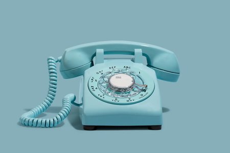 A vintage blue rotary desk phone on a blue background