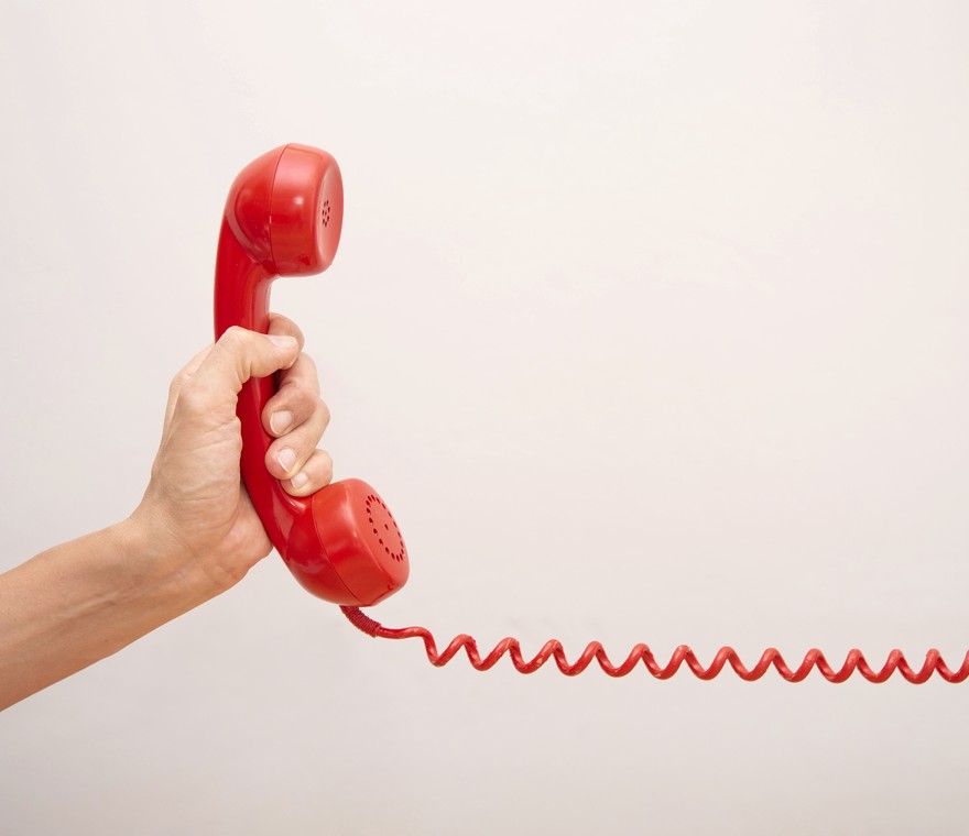 A hand holding a red telephone receiver with a long coiled cord